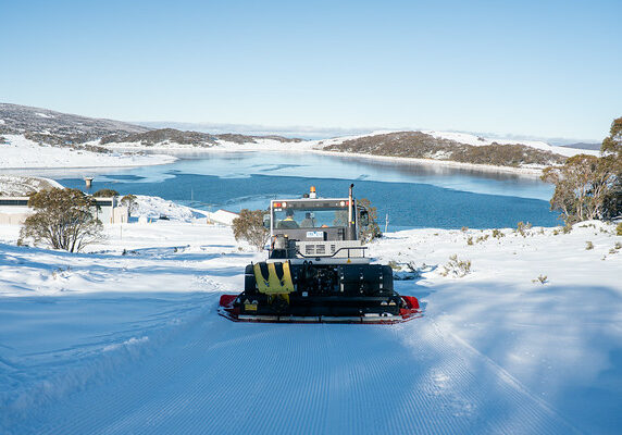 A trail groomer on it's way down a snowy cross country ski trail with Rockey Valley Lake in the background.